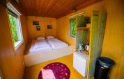 Intérieur chaleureux de la tiny house Pipowagen avec deux lits, kitchenette et fenêtres donnant sur la nature.
