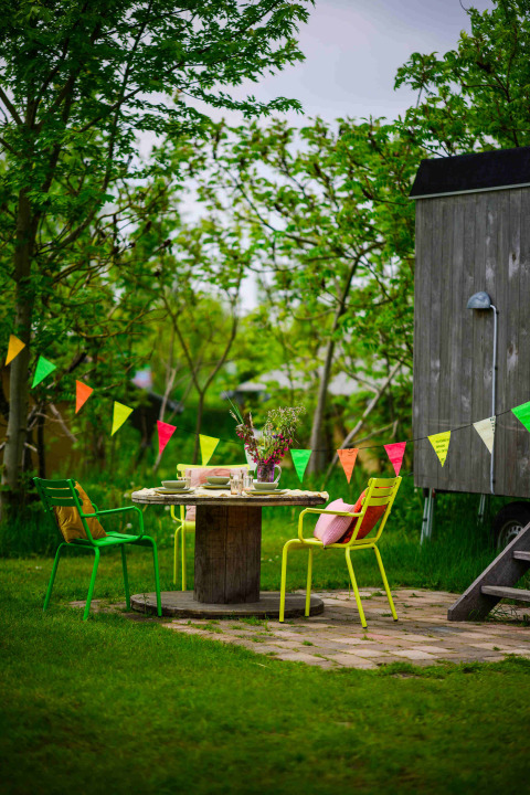 Mesa exterior colorida con sillas y banderines junto a una cabaña de madera en Netl Camping Kallumaan, Países Bajos.
