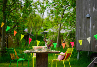 Mesa exterior colorida con sillas y banderines junto a una cabaña de madera en Netl Camping Kallumaan, Países Bajos.