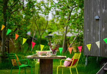 Bunter Gartentisch mit Stühlen und Girlanden neben einem Holzhaus im Netl Camping Kallumaan, Niederlande.