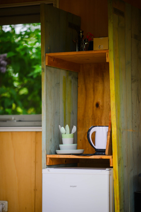 Et køkkenskab i et tiny house ved Pipowagen, Netl Camping Kallumaan, med elkedel, kopper og tallerkener.