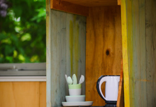 Placard ouvert dans une tiny house à Pipowagen, Netl Camping Kallumaan, avec bouilloire, tasses et assiettes.