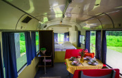 Binnenkant van de Streetcar tiny house bij Netl Camping Kallumaan, met bed, tafel en blauwe gordijnen.