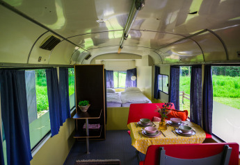 Indretning af Streetcar tiny house på Netl Camping Kallumaan, med spisebord, seng og blå gardiner.