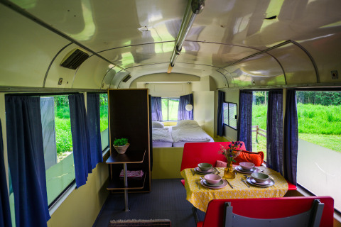 Indretning af Streetcar tiny house på Netl Camping Kallumaan, med spisebord, seng og blå gardiner.