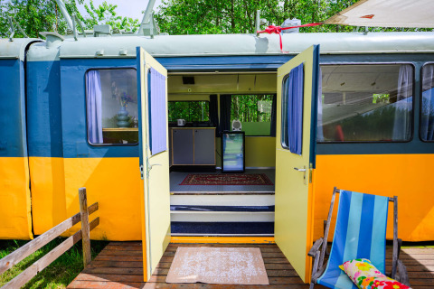 Minicasa Streetcar en Netl Camping Kallumaan, Países Bajos, con puertas abiertas mostrando el interior.