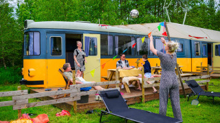 Gezin geniet buiten voor het tiny house Streetcar met tuinstoelen en vrolijke vlaggetjes.
