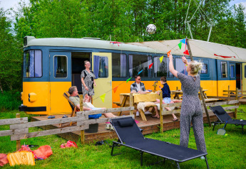 Gezin zit buiten bij tiny house Streetcar met tuinmeubilair en kleurrijke slingers in het groen.