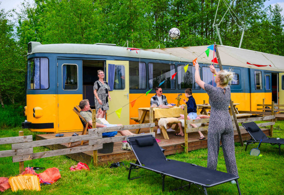 Gezin zit buiten bij tiny house Streetcar met tuinmeubilair en kleurrijke slingers in het groen.