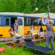 Familia disfrutando al aire libre frente a la tiny house Streetcar con muebles de jardín y banderines.