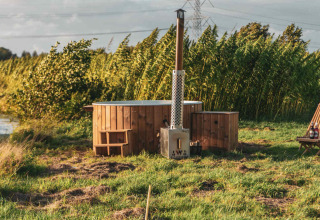 Bañera de madera al aire libre junto a una tiny house, en césped verde y rodeada de vegetación alta.