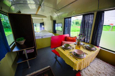 Interieur van tiny house Streetcar op Netl Camping Kallumaan, met eettafel, bed en uitzicht op het groen.