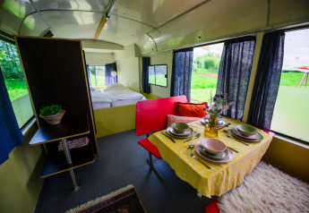 Interieur van tiny house Streetcar op Netl Camping Kallumaan, met eettafel, bed en uitzicht op het groen.