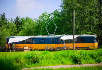 Tiny house in oude tram bij Netl Camping Kallumaan in Nederland, omringd door gras en bomen.