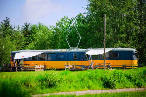 Streetcar tiny house at Netl Camping Kallumaan in the Netherlands, surrounded by green grass and trees.