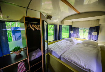 Streetcar tiny house met tweepersoonsbed en kast bij Netl Camping Kallumaan in Nederland, uitzicht op bos.