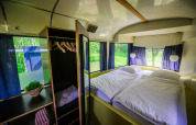 Streetcar tiny house with double bed and wardrobe at Netl Camping Kallumaan in the Netherlands, forest view.