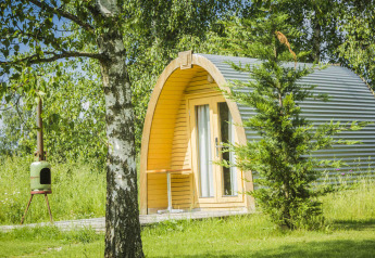 Pod Log Cabin al Netl Camping Kallumaan nei Paesi Bassi, circondato da alberi e prato verde estivo.