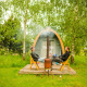 To personer sidder foran en træhytte ved Log Cabin pod, omgivet af grønne træer og natur.