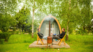 Dos personas se relajan frente a una cabaña llamada Log Cabin, rodeadas de árboles y césped verde.