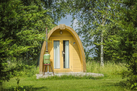 Una foto de la cabaña Log Cabin en Netl Camping Kallumaan, Países Bajos, rodeada de césped y árboles verdes.