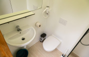 Modern tiny house bathroom with sink, wall toilet, mirror, and hairdryer at Netl Camping Kallumaan.