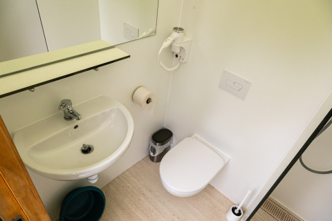 Modern tiny house bathroom with sink, wall toilet, mirror, and hairdryer at Netl Camping Kallumaan.