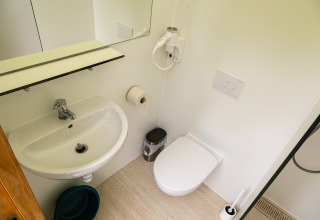 Petite salle de bain moderne avec lavabo, WC mural, miroir et sèche-cheveux à Netl Camping Kallumaan.