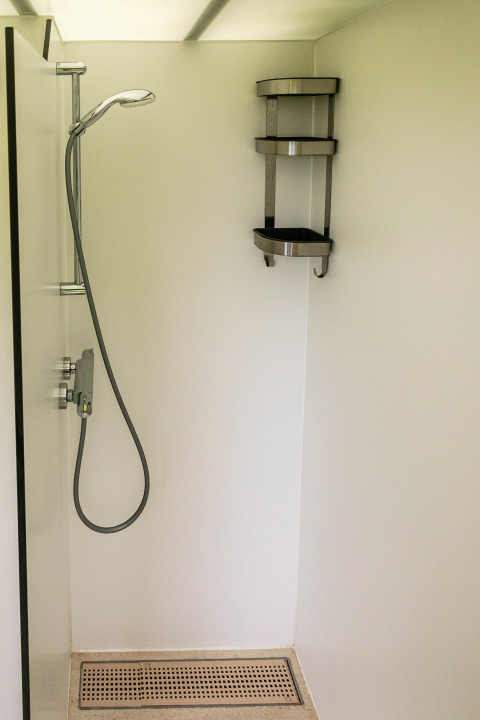 Douche minimaliste à Birdhouse, Netl Camping Kallumaan, Pays-Bas, avec étagère d’angle en acier inoxydable.