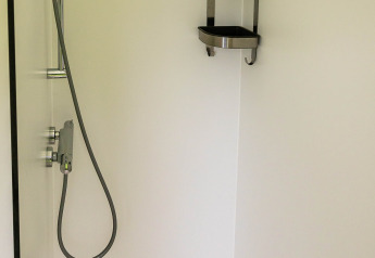 Douche minimaliste à Birdhouse, Netl Camping Kallumaan, Pays-Bas, avec étagère d’angle en acier inoxydable.