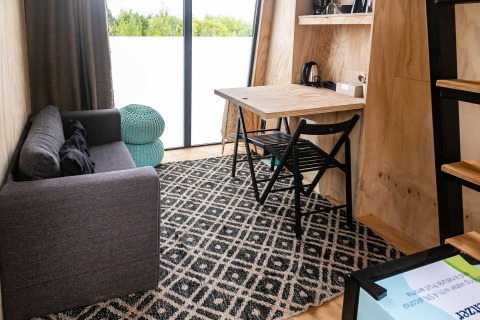 Moderne og hyggelig stue inde i Birdhouse, Netl Camping Kallumaan, med sofa, bord og stort vindue.