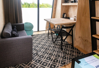 Intérieur douillet du Birdhouse à Netl Camping Kallumaan, Pays-Bas, avec canapé, bureau et grande fenêtre.