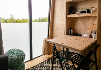 Interior de tiny house con mesa de madera, sillas y ventanales en Birdhouse, Netl Camping Kallumaan, Países Bajos.