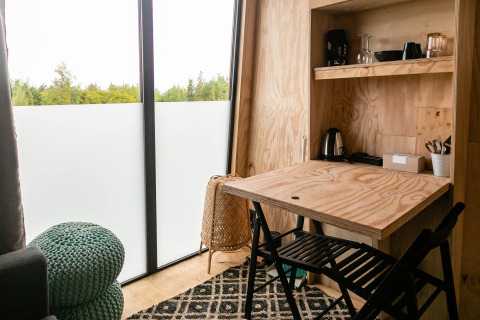 Interno di tiny house con tavolo in legno, sedie e finestre al Birdhouse, Netl Camping Kallumaan, Paesi Bassi.