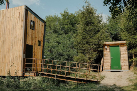 Træbeklædt tiny house Birdhouse med rampe ved Netl Camping Kallumaan, omgivet af grønne træer i Holland.