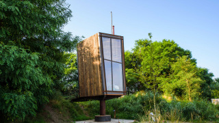 Una tiny house chiamata Birdhouse, rialzata su una colonna, circondata da vegetazione verde e alberi.
