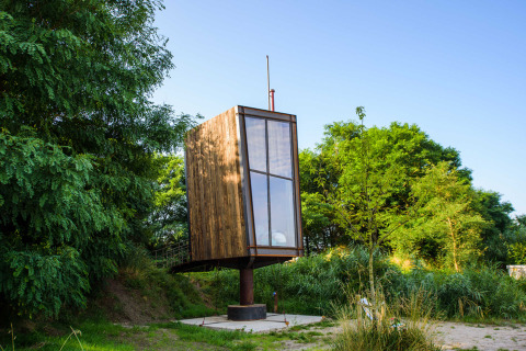 Tiny house nommée Birdhouse, surélevée sur un pilier et entourée de verdure et d’arbres luxuriants.