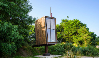 Una tiny house llamada Birdhouse, elevada sobre un pilar y rodeada de vegetación verde y árboles.
