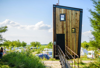A modern, narrow tiny house called Birdhouse at Netl Camping Kallumaan surrounded by tents in the Netherlands.