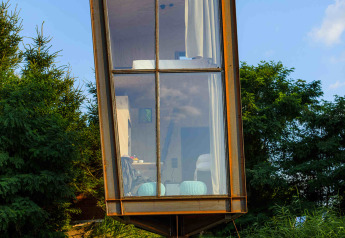 Pequeña casa Birdhouse elevada en Netl Camping Kallumaan, Países Bajos, con gran ventanal frontal.