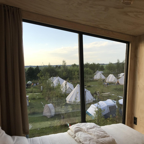Uitzicht vanuit het Birdhouse tiny house op tenten en natuur bij Netl Camping Kallumaan in Nederland bij zonsondergang.