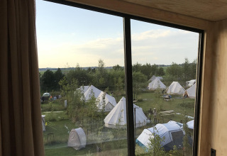 View from Birdhouse tiny house over tents and greenery at Netl Camping Kallumaan in the Netherlands at sunset.