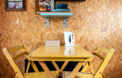 Petit coin repas avec table et chaises jaunes, décor mural et vaisselle dans une tiny house en conteneur aux Pays-Bas.