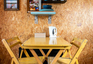 Knus eethoekje met gele stoelen en tafel, wanddecoratie en serviesrek in een tiny house container in Nederland.
