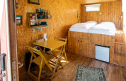 Indvendig visning af en lille containerhus med trægulv, spisebord og dobbeltseng i Netl Camping Kallumaan.