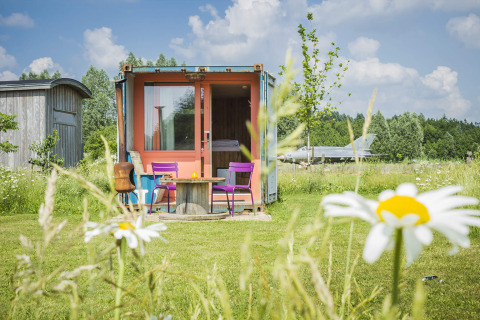 Farverig shipping container tiny house ved Netl Camping Kallumaan i Holland, omgivet af blomster og natur.