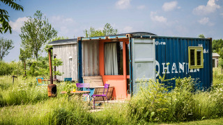 Une tiny house colorée construite à partir d'un conteneur maritime, entourée de fleurs sauvages et d'herbe.