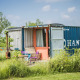 Et farverigt tiny house bygget af en shipping container, omgivet af grønt græs og vilde blomster.