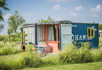 Une tiny house colorée construite à partir d'un conteneur maritime, entourée de fleurs sauvages et d'herbe.