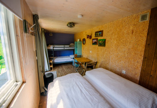 Helles Tiny House mit Etagenbett, Doppelbett, kleinem Tisch und großen Fenstern mit Blick ins Grüne.